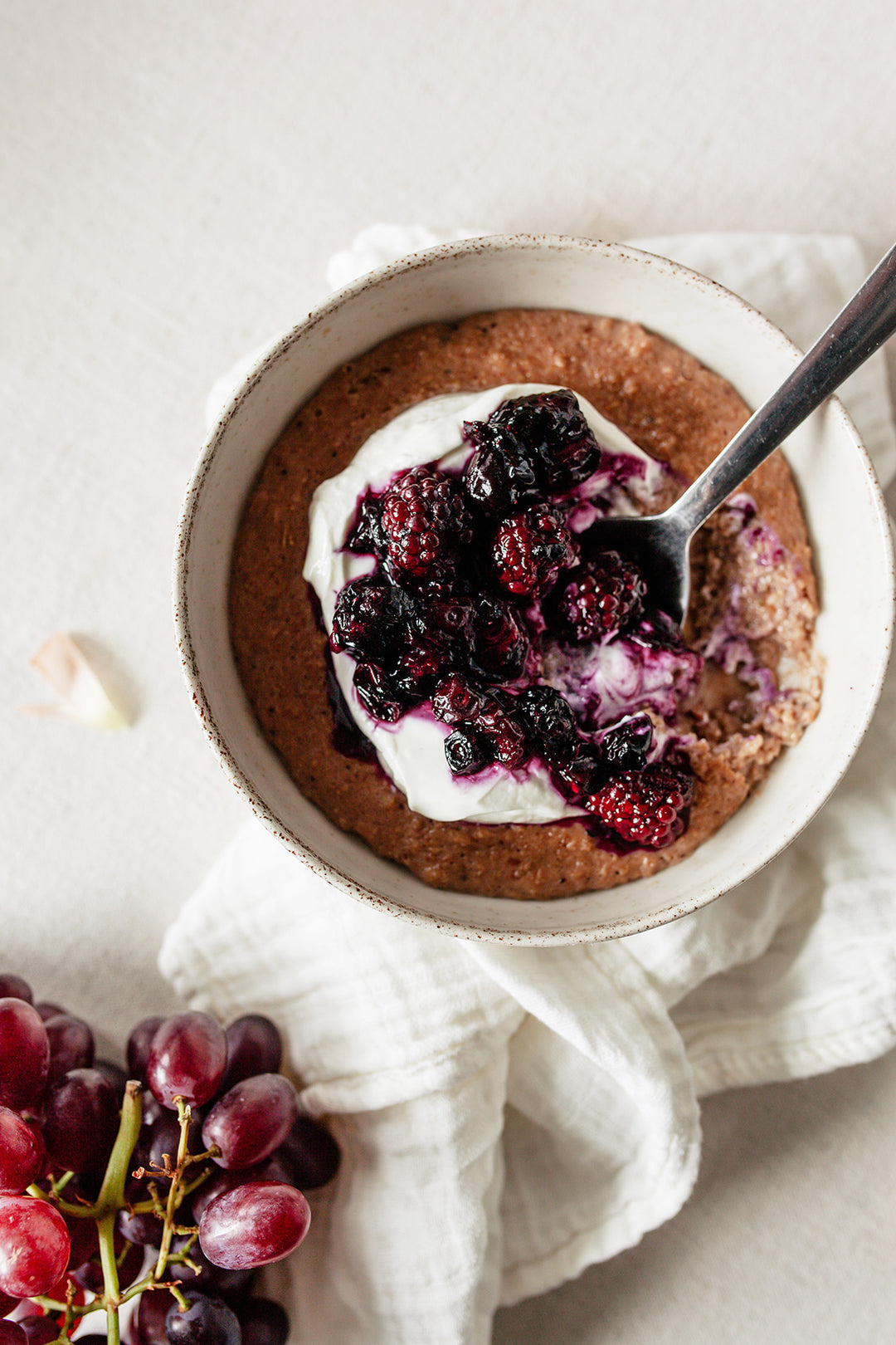 A bowl of warm, gluten-free porridge topped with yogurt, blackberry, and blueberry compote