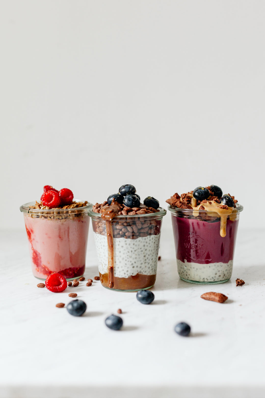 Three healthy smoothie and chia pudding parfait options with toppings of fresh fruit, cereals, granola and nut butter