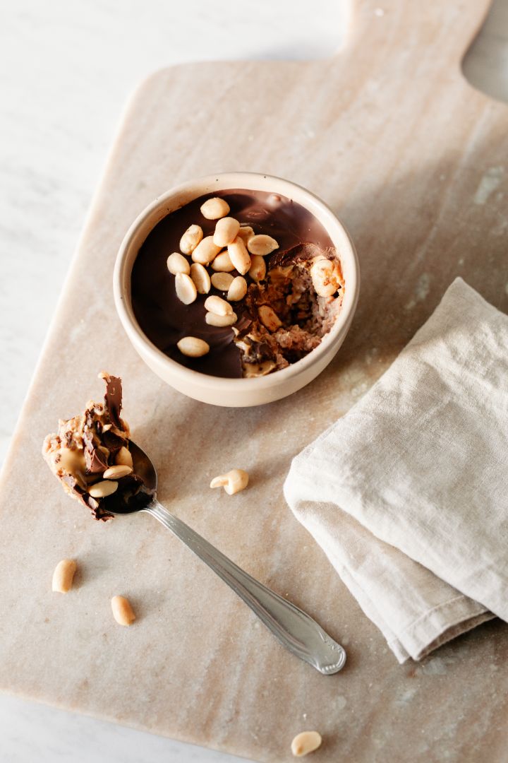 Een kom gezonde overnight oats met chocolade en pindakaas, bedekt met een harde chocoladelaag en geroosterde pinda's 